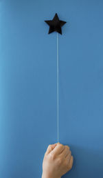 Cropped hand holding thread hanging from star shape against blue background