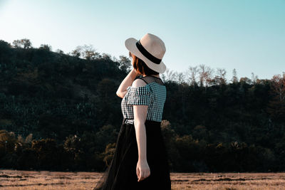 Woman wearing hat standing on field against sky