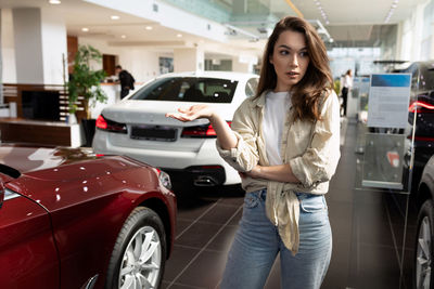 Portrait of young woman standing against car