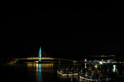 Illuminated bridge over river against sky at night
