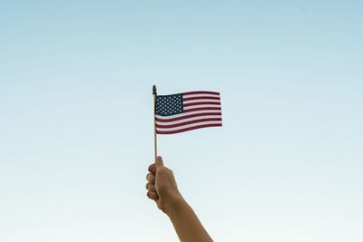 Low angle view of hand holding flag against clear sky