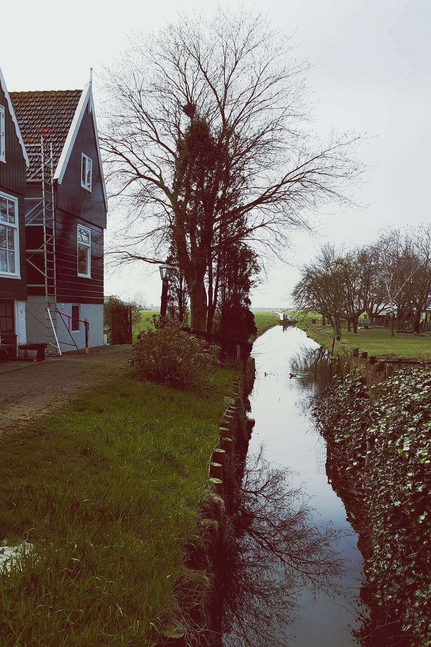 tree, water, grass, bare tree, tranquility, built structure, reflection, architecture, tranquil scene, nature, building exterior, sky, growth, clear sky, field, branch, canal, beauty in nature, scenics, lake