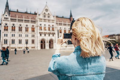 Rear view of woman photographing building in city