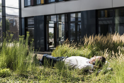 Businessman with headphones lying on a bench outside office building