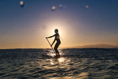 Female sup surfer at sunset time