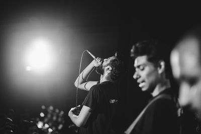 Side view of young man singing passionately at a live rock concert while facing the audience 