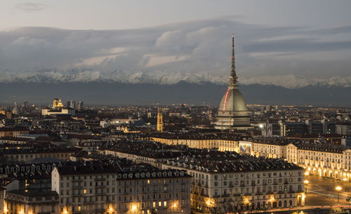 Illuminated buildings in city against cloudy sky