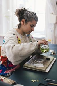 Female craftsperson holding jar while making jewelry at home