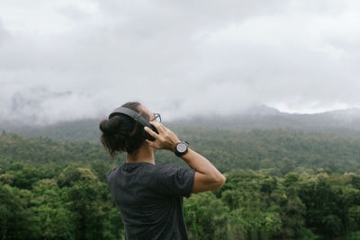 Man listening music while standing against mountains and sky