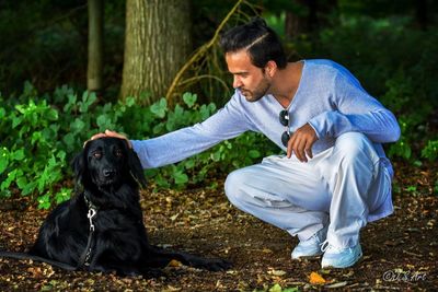 Young man stroking dog while crouching on field