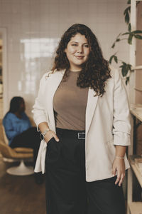 Portrait of confident businesswoman standing with hand in pocket at office