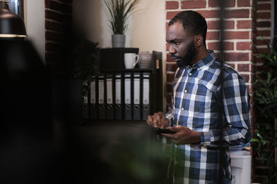 Side view of young man standing against window