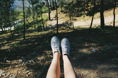 Low section of woman wearing shoes against trees