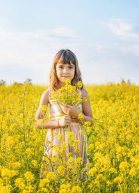 Portrait of smiling young woman standing amidst yellow flowering plants on field against sky