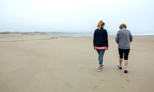 Rear view of mother and daughter walking at beach against sky