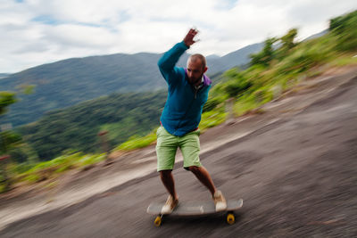 Full length of mid adult man skateboarding on mountain against sky