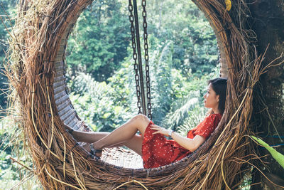 Thoughtful woman sitting on swing in forest