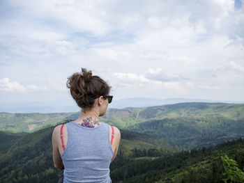 Rear view of woman looking at mountains against cloudy sky