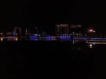 Illuminated buildings by river against sky at night