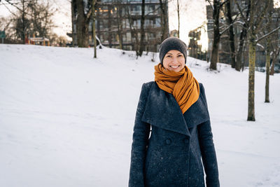 Smiling woman in a winter coat, scarf and hat against the backdrop of a winter snowy city