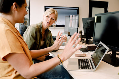 Female business professionals discussing over laptop while sitting at desk in office