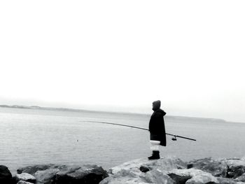 Rear view of man fishing in sea against clear sky