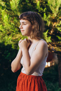 Young woman looking away while standing against trees