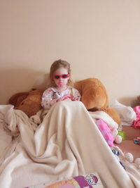 Portrait of girl in sunglasses sucking pacifier while leaning on bed at home