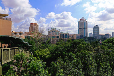 Trees and buildings in city against sky