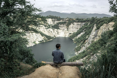 Rear view of man sitting on mountain against sky