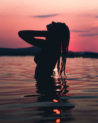 Silhouette woman in sea against sky during sunset