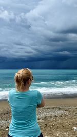 Rear view of woman standing at beach against sky