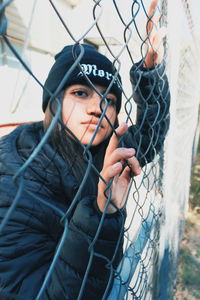 Portrait of young woman standing by chainlink fence