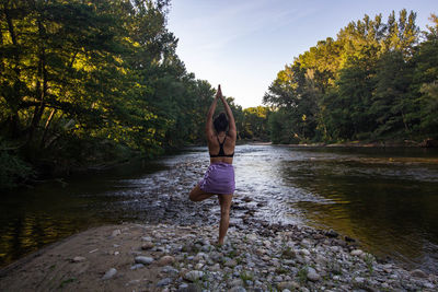 Rear view of woman standing by lake against trees