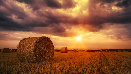 Hay bales on field against cloudy sky at sunset