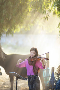Portrait of young woman playing violin by horse