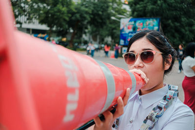 Portrait of woman wearing sunglasses while holding traffic cone