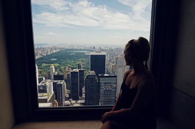 Woman looking through window against city