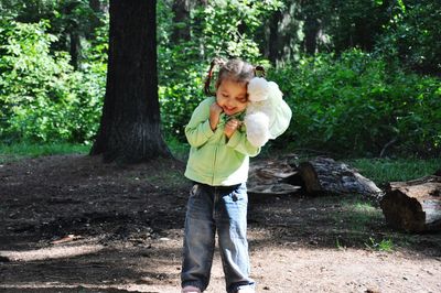 Full length of a girl holding tree trunk in forest