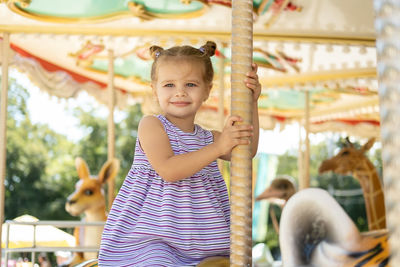 Funny little kid girl in colorful dress rides on carousel in an amusement park in summer day