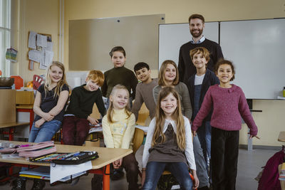 Portrait of smiling teacher and girls and boys against whiteboard in classroom