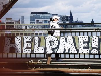 Man standing on bridge against sky in city