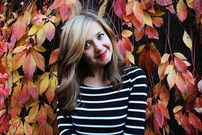 Portrait of young woman standing against autumn leaves