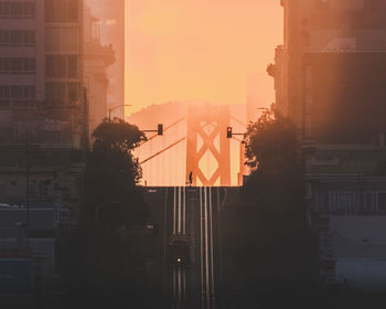 Silhouette of standing by buildings against sky during sunset