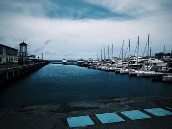 Boats moored at harbor against sky in city