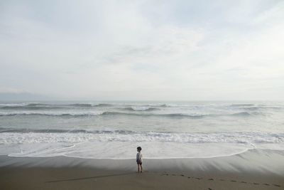 Rear view of woman standing on beach against sky