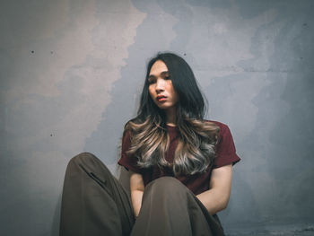 Beautiful young woman sitting against wall