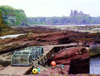 Lobster traps on wall against rocky shore with tantallon castle in background