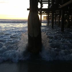 Sea waves splashing on beach against sky during sunset
