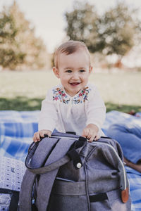 Cute baby girl sitting by bag on picnic blanket